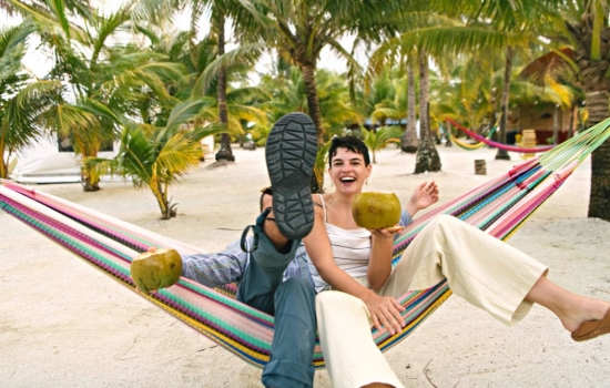 Couple enjoying Glover's Reef on a hammock while sipping on a coconut